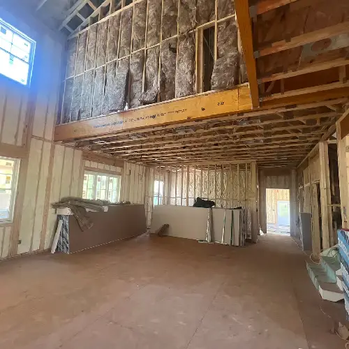 A spacious room under construction, featuring exposed wooden beams, insulation, and unfinished walls