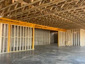Interior view of a building with newly framed wooden walls on a concrete floor beneath an unfinished wood truss ceiling