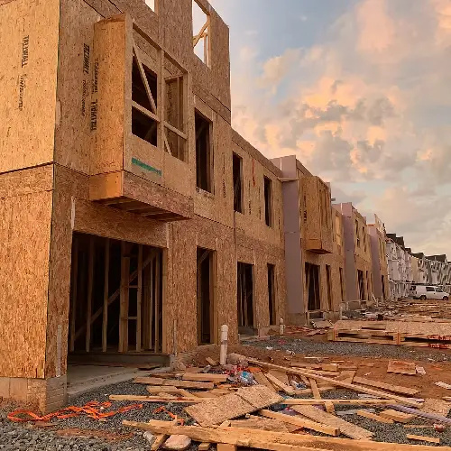 Newly constructed townhomes in progress, featuring wood framing and exposed structures, under a colorful sky at sunset